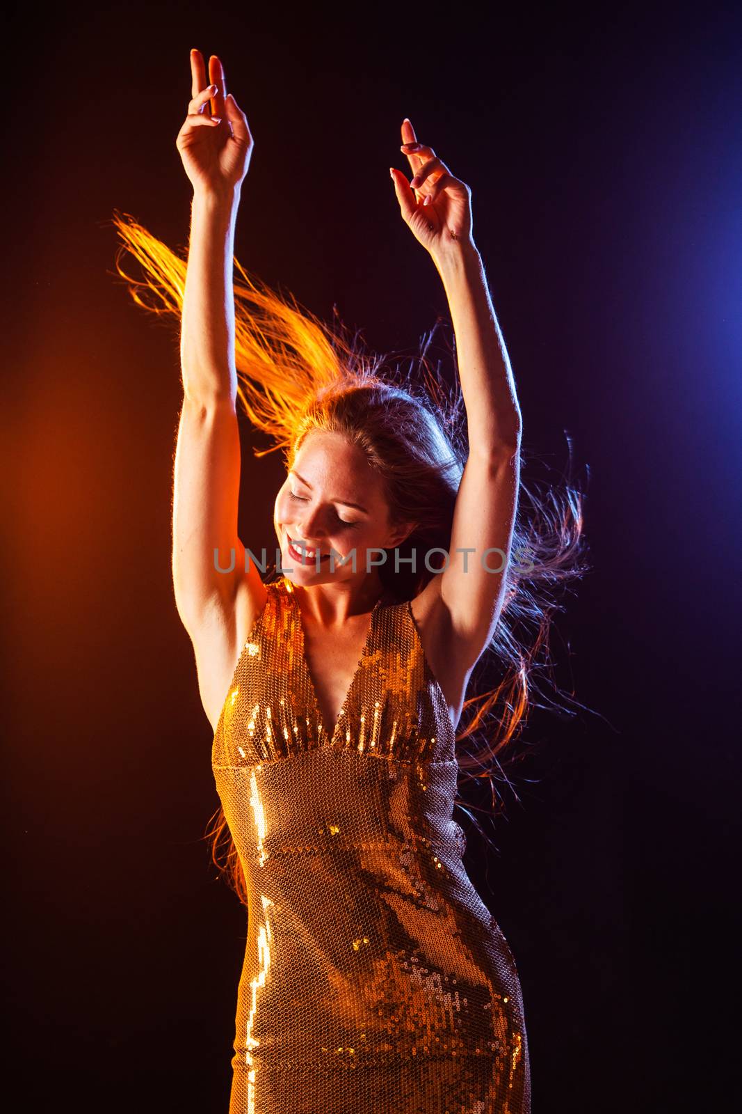 Portrait of dancing girl in golden dress on disco party blue and red studio lights