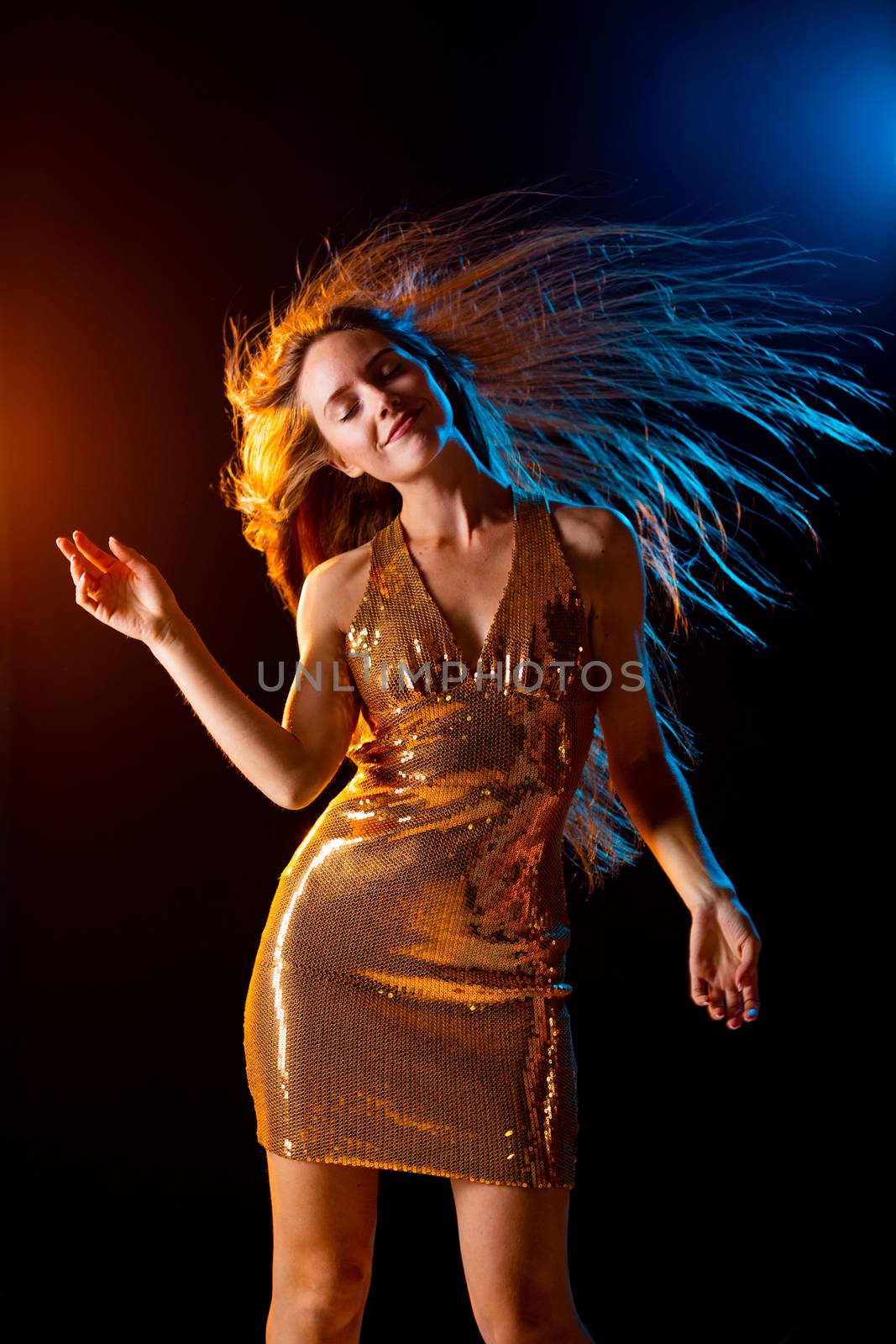 Portrait of dancing girl in golden dress on disco party blue and red studio lights