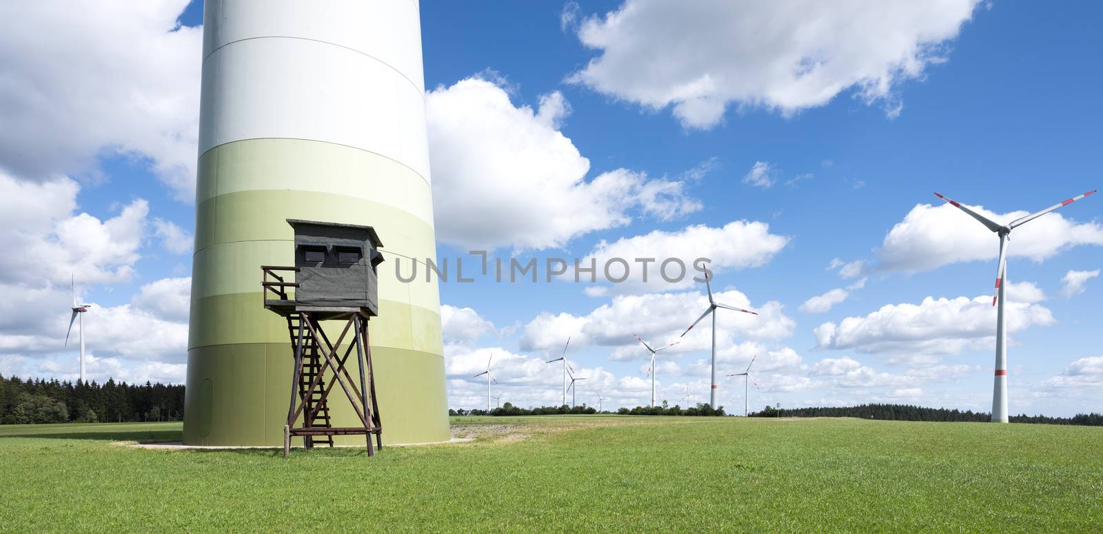 wind turbines and high seat in german eifel in green grass with blue sky and white clouds by ahavelaar