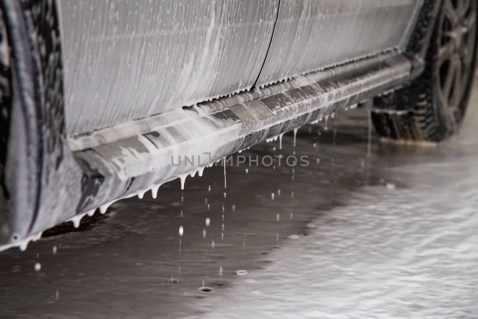 close-up view of silver car step at carwash with soap sud smudges and drops.