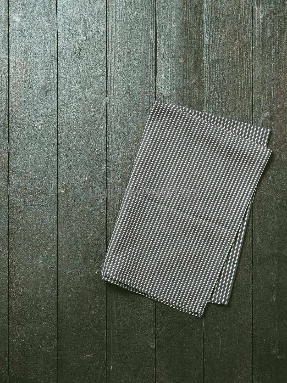 Dark wooden table with balck and white dark linen kitchen towel or textile napkin flat lay. Dark tablecloth on brown gray wood tabletop. Copy space for text. Can use as mock up for design. Vertical.