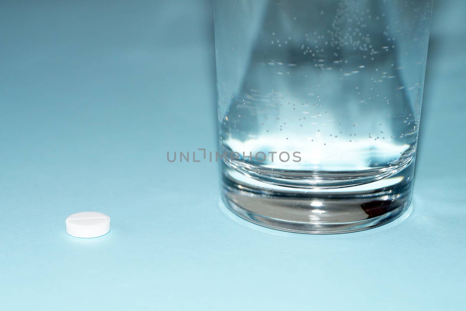 pill and glass of water on blue background close-up