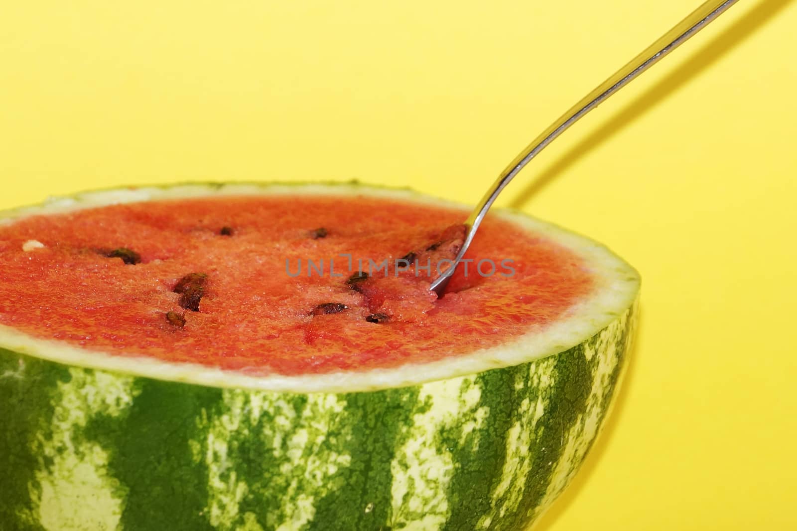 half watermelon with a spoon on a yellow background close-up by Annado