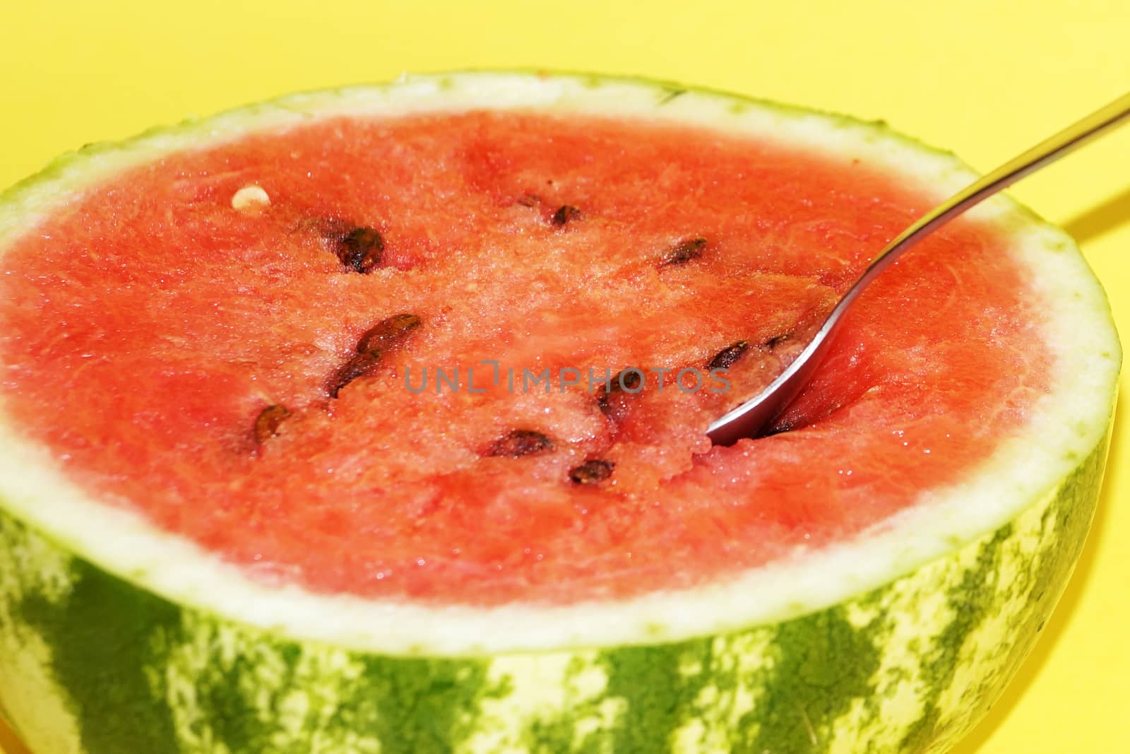 half watermelon with a spoon on a yellow background close up