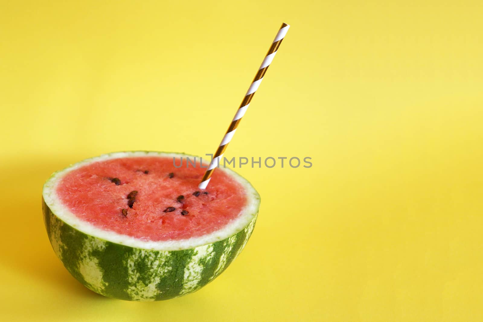 half watermelon with cocktail straw on yellow background, close up