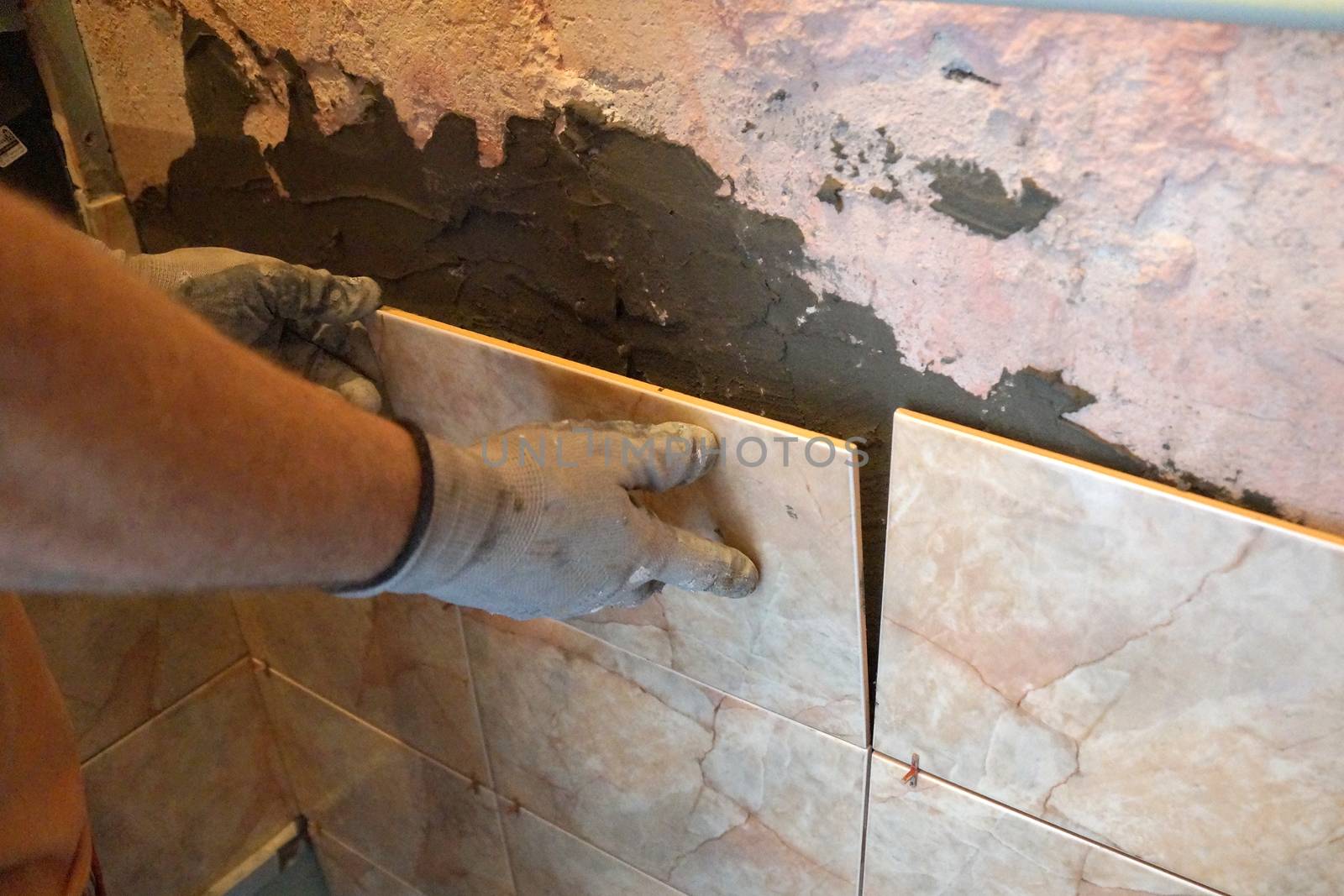 a man laying ceramic tiles on the wall close-up by Annado