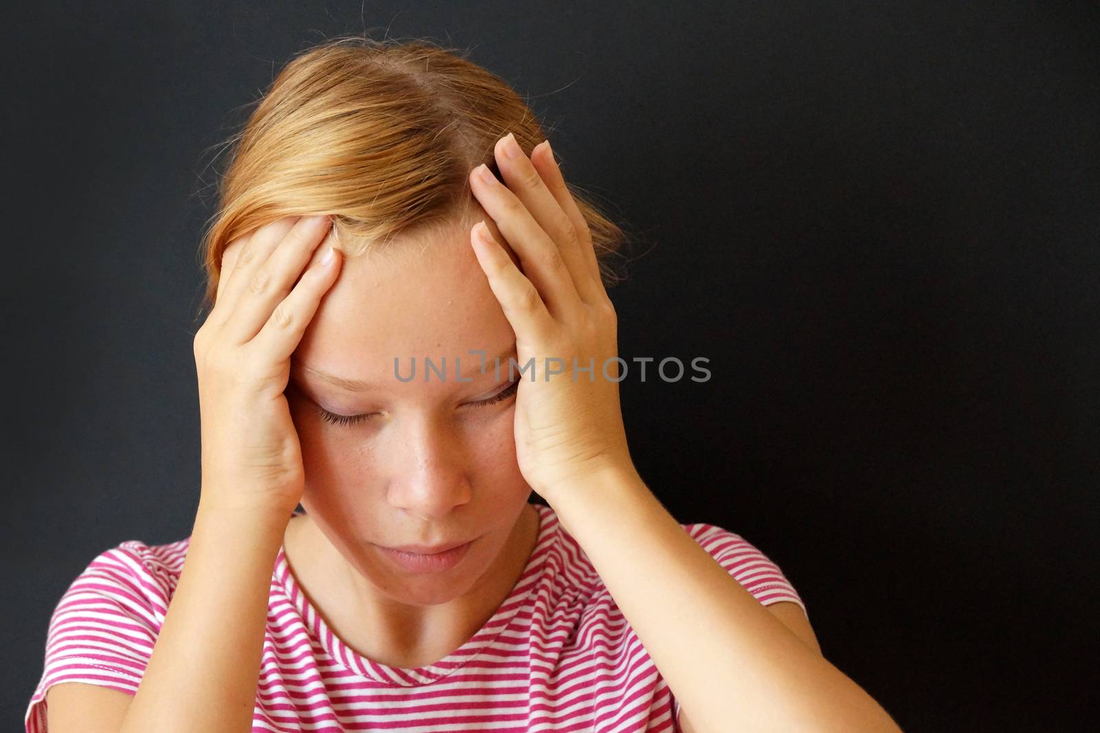 teenage girl with closed eyes holds her sore head with her hands.