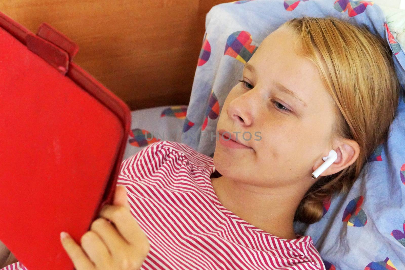 teenage girl in headphones looking tablet while lying in bed by Annado