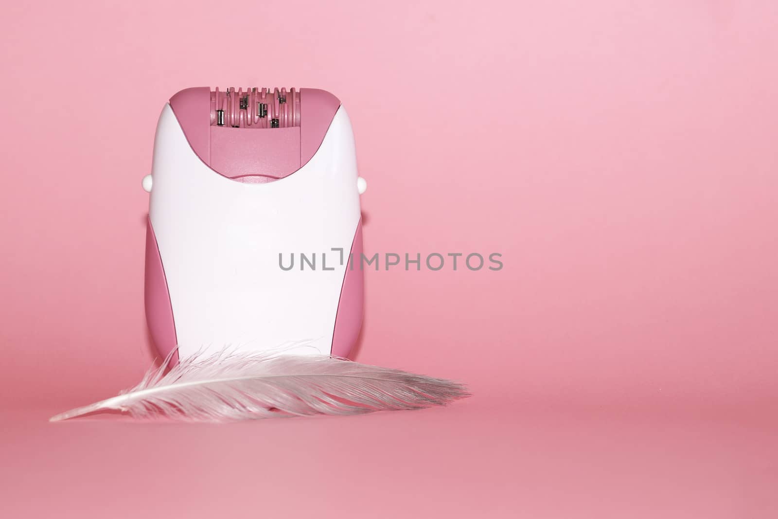 electric handheld epilator and feather on pink background close-up