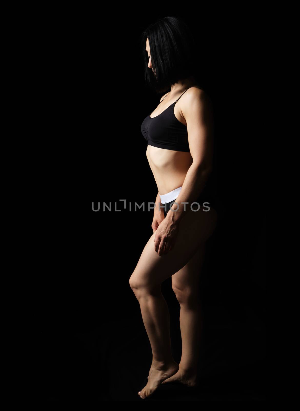 adult caucasian appearance woman in a black bra and bikini stands on a black background, beautiful muscular body, short haircut