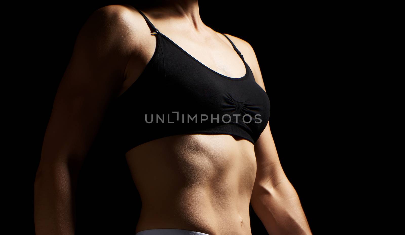 muscular abs on the stomach of a caucasian woman in a black bra, low key