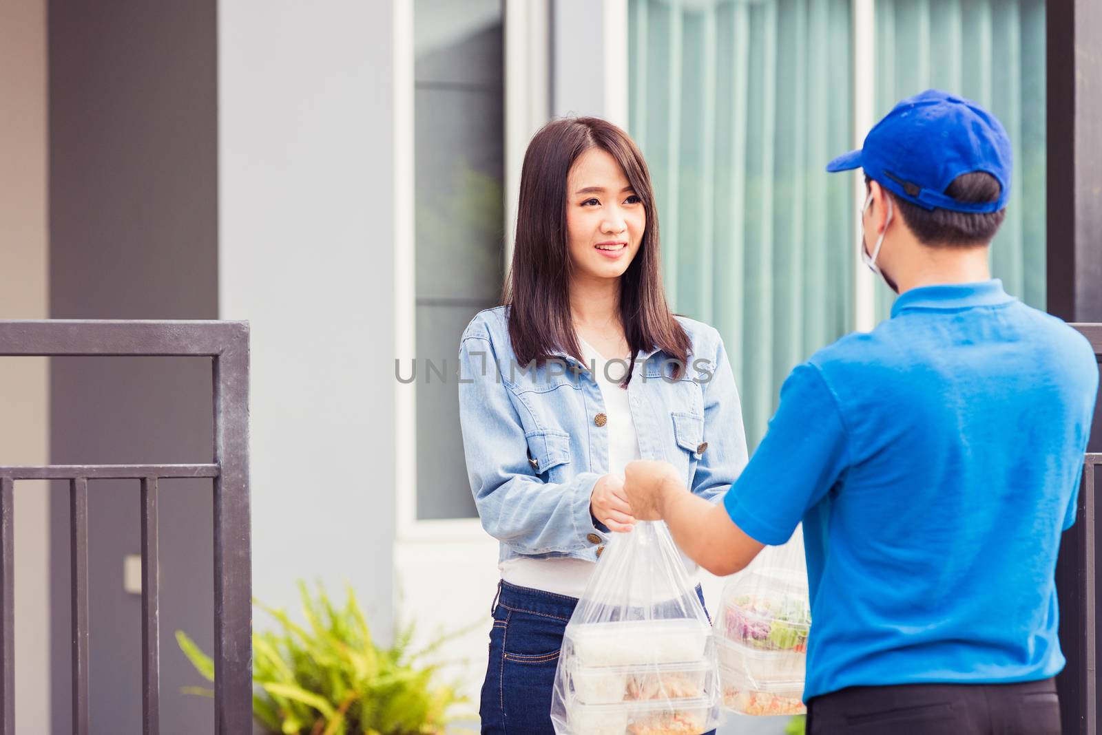 Asian young delivery man wear face mask he making grocery service giving rice food boxes plastic bags to woman customer receiving door at house after pandemic coronavirus, Back to new normal concept