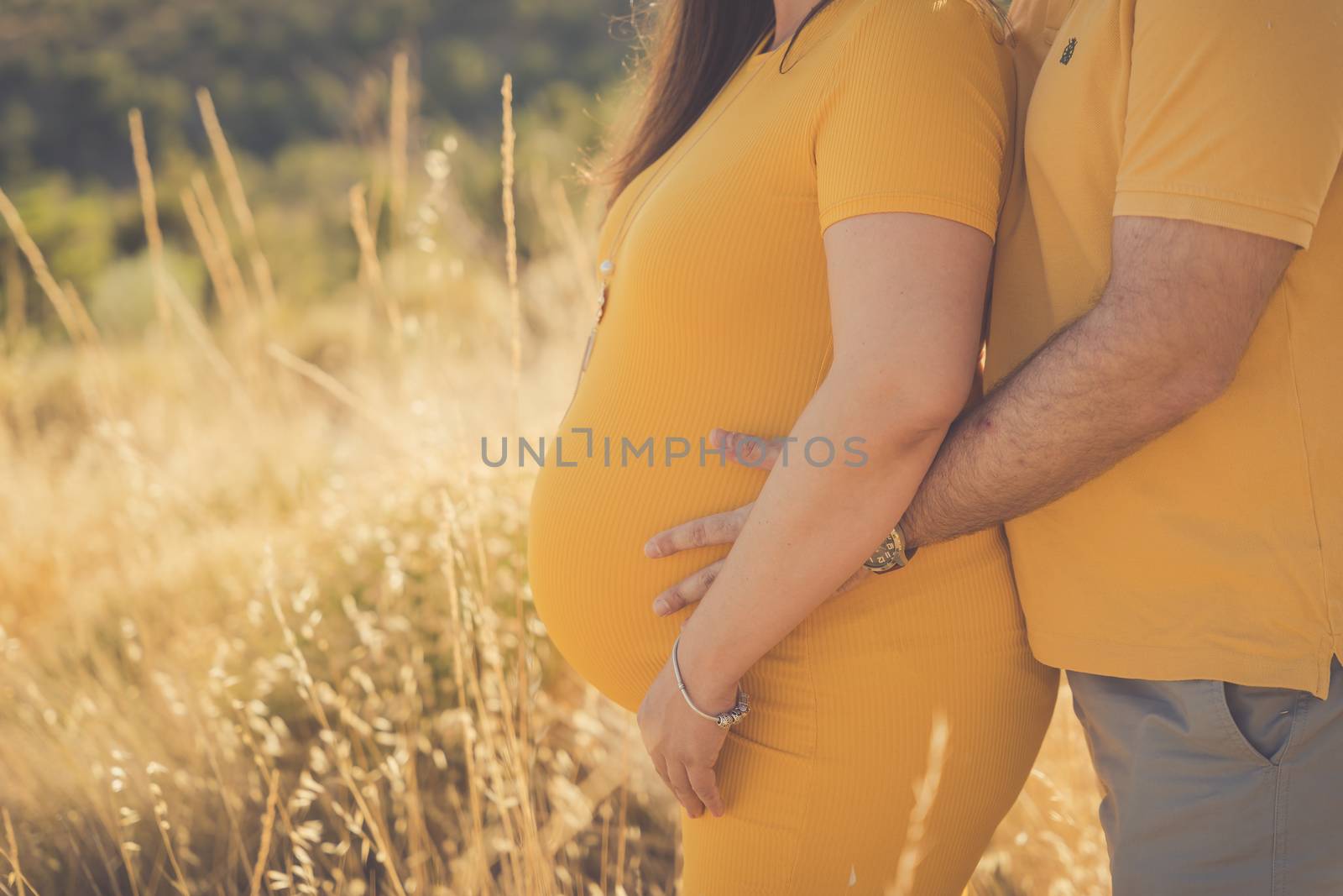 Side view pose of expecting couple, their hands holding the pregnant mother's belly. Isolated on white.