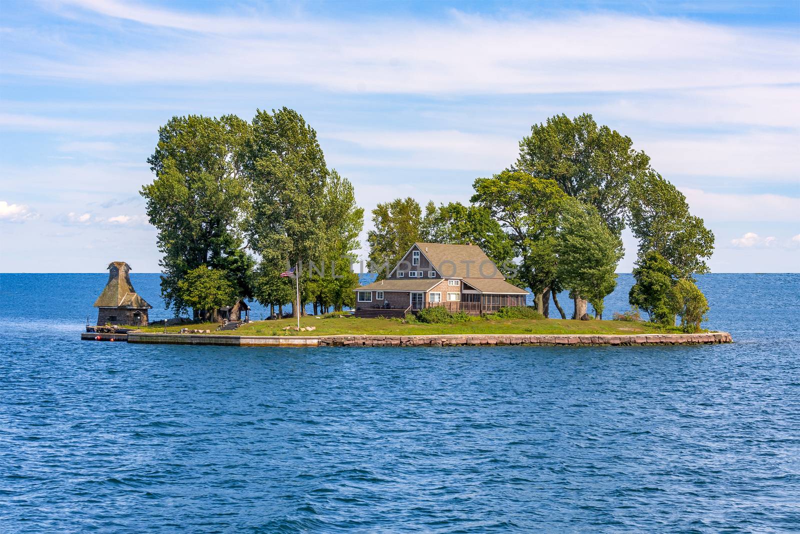 A beautiful house and a couple of large trees fit on a small island in the middle of a large lake