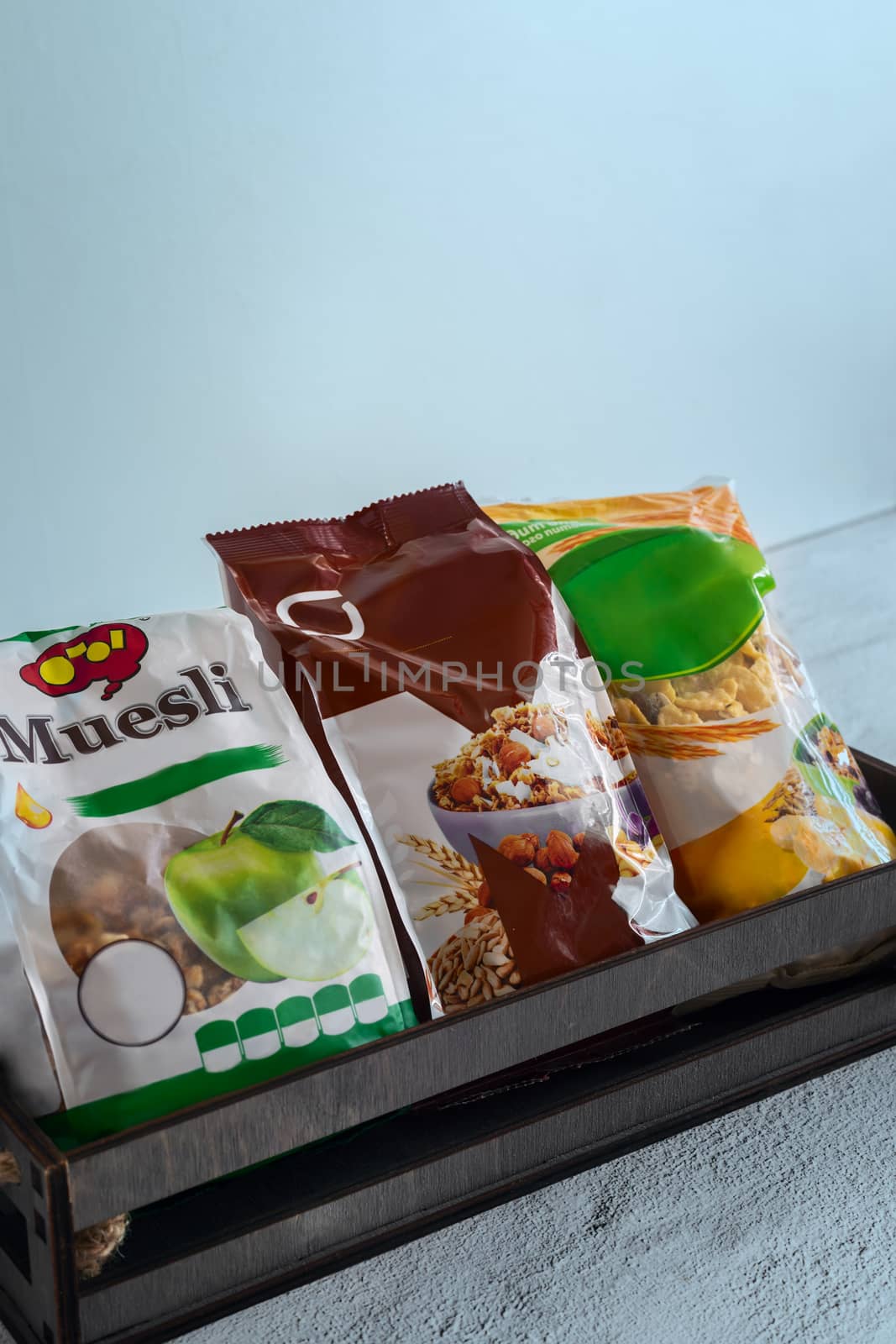 On the table in a wooden container, three packages of muesli in cellophane bags.
