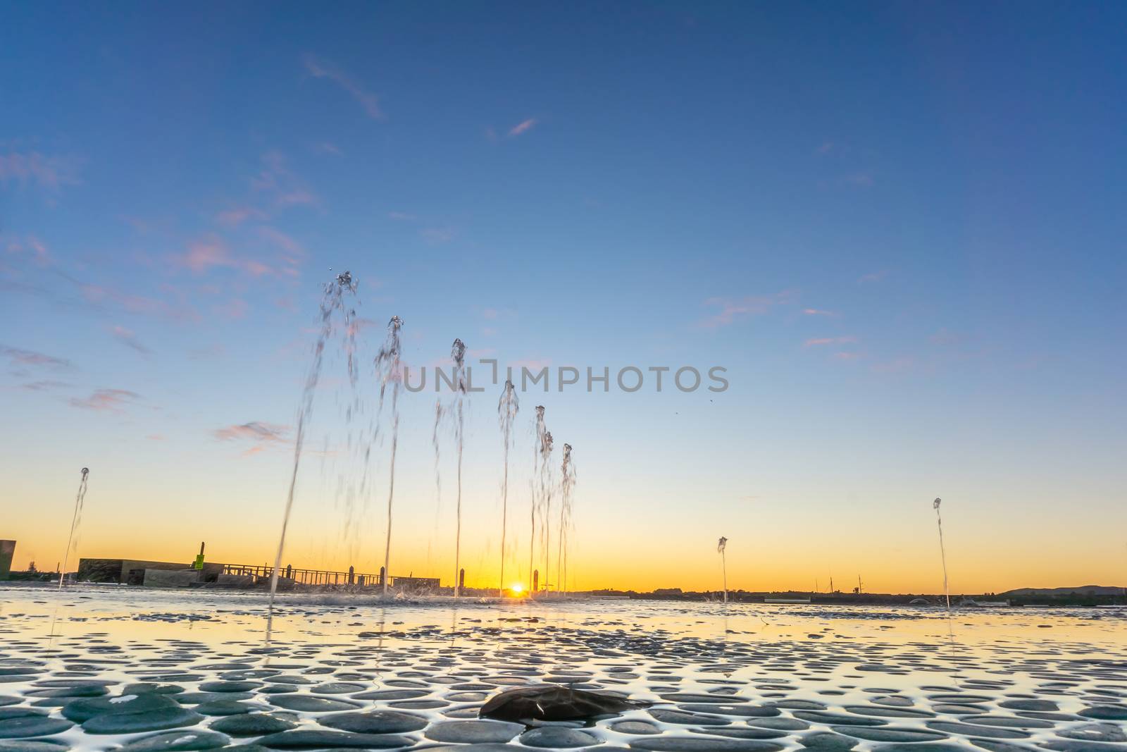 Water feature with spraying water on Tauranga Strand waterfront at sunrise with clear blue sky, New Zealand