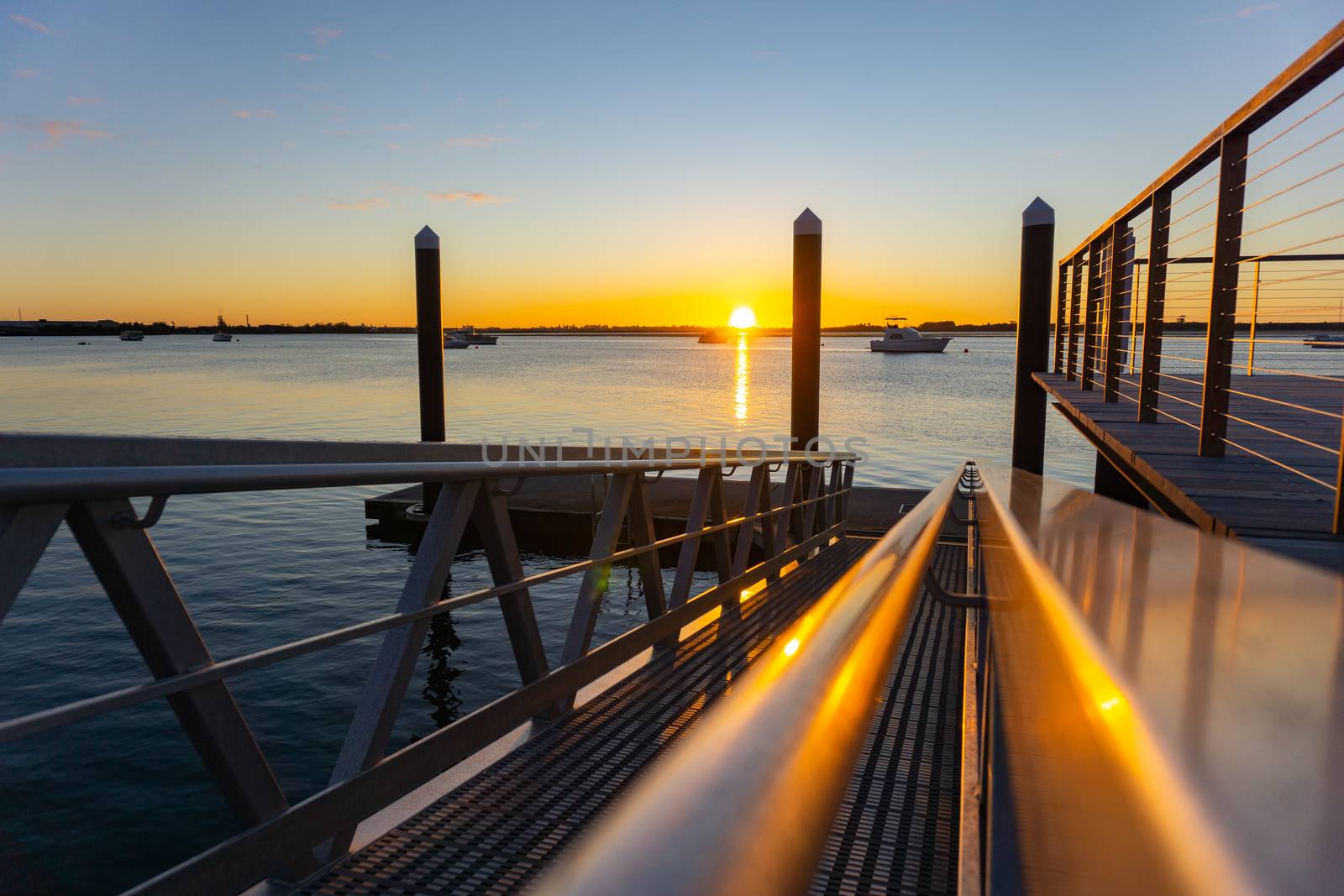 Sunrise glows on horizon and pier railings leading to harbor. by brians101