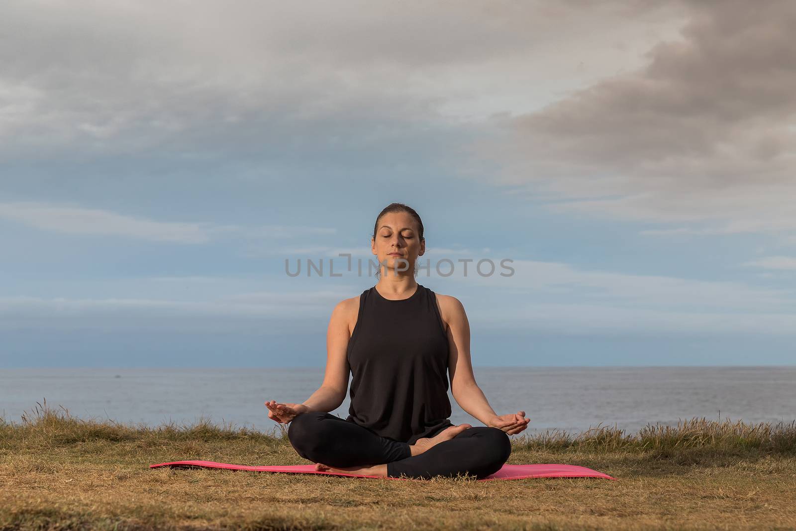 Woman doing yoga outdoors with the sea in the background. by JRPazos