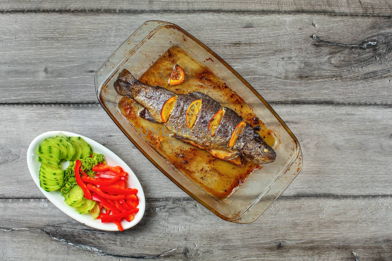 Table top view on grilled trout with lemons in glass baking pan, by Ivanko