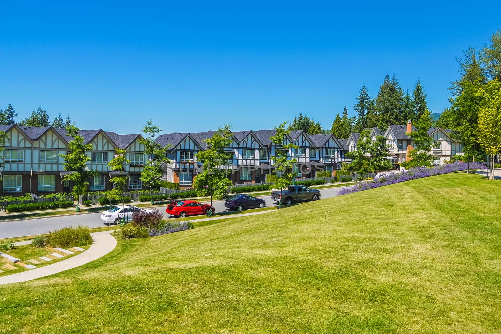 Row of new townhouses with recreation area across the road and parked car on the road