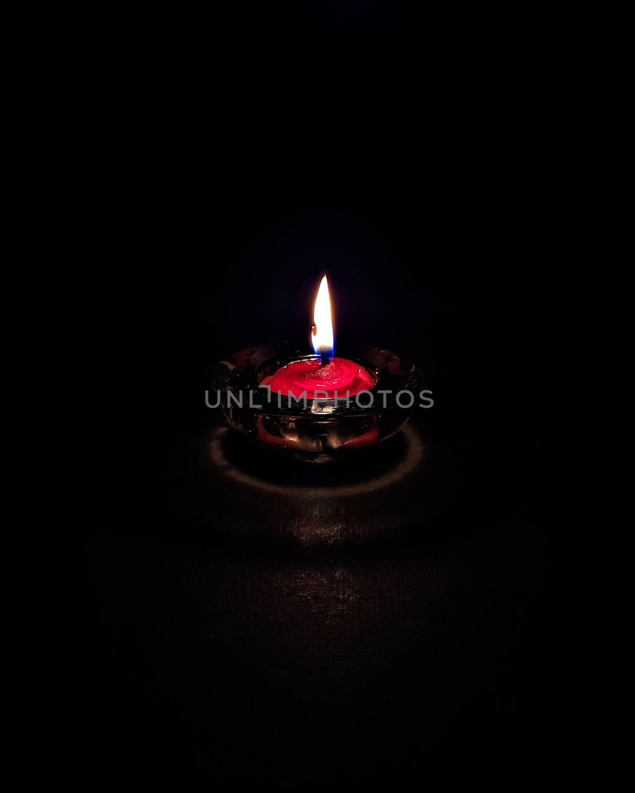Isolated,close up image of small red colored wax lamp(Diya) burning in dark night with steady yellow,blue flame.