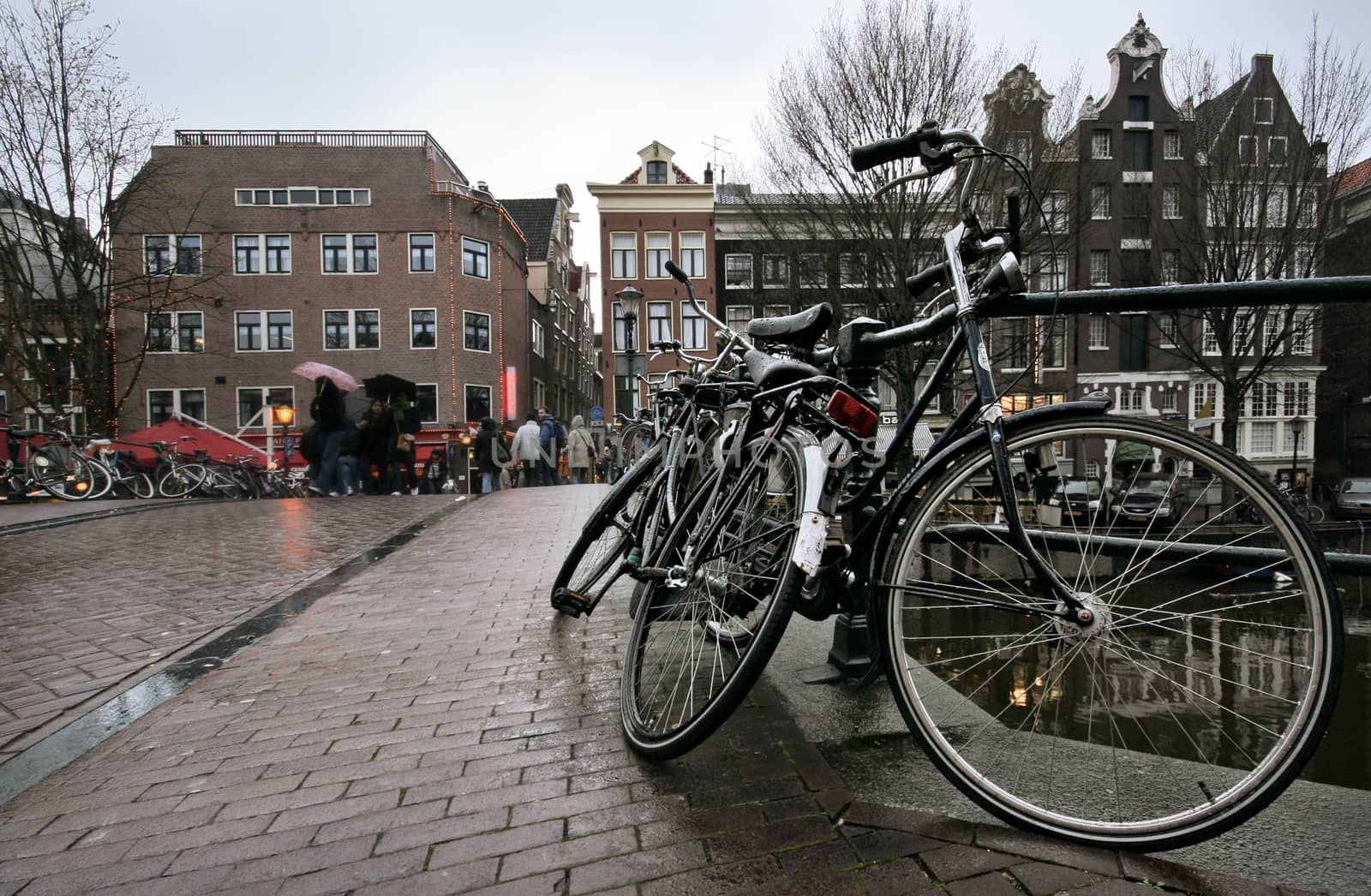 Amsterdam, Netherlands - March 23, 2008: black bicycles wet from rain parked on bridge over one of many canals with houses in the back. 