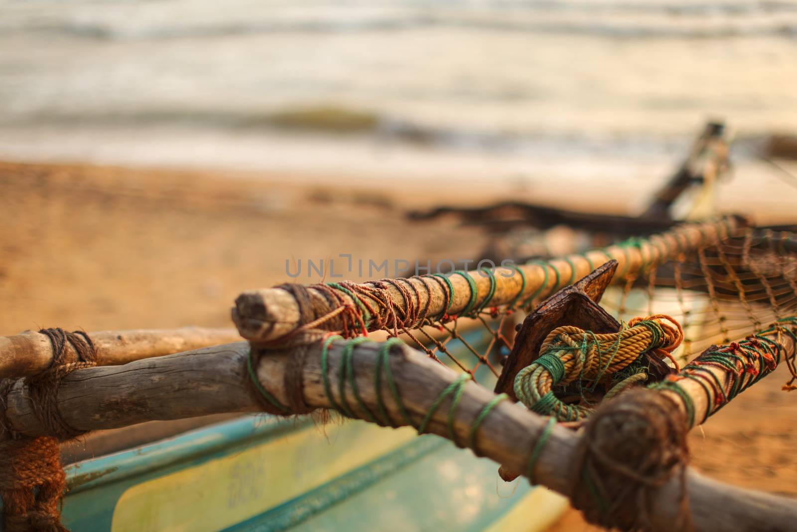 Detail on wooden poles, ropes, nets and metal anchor on old fishing boat laying on beach during sunset. Kalutara, Sri Lanka