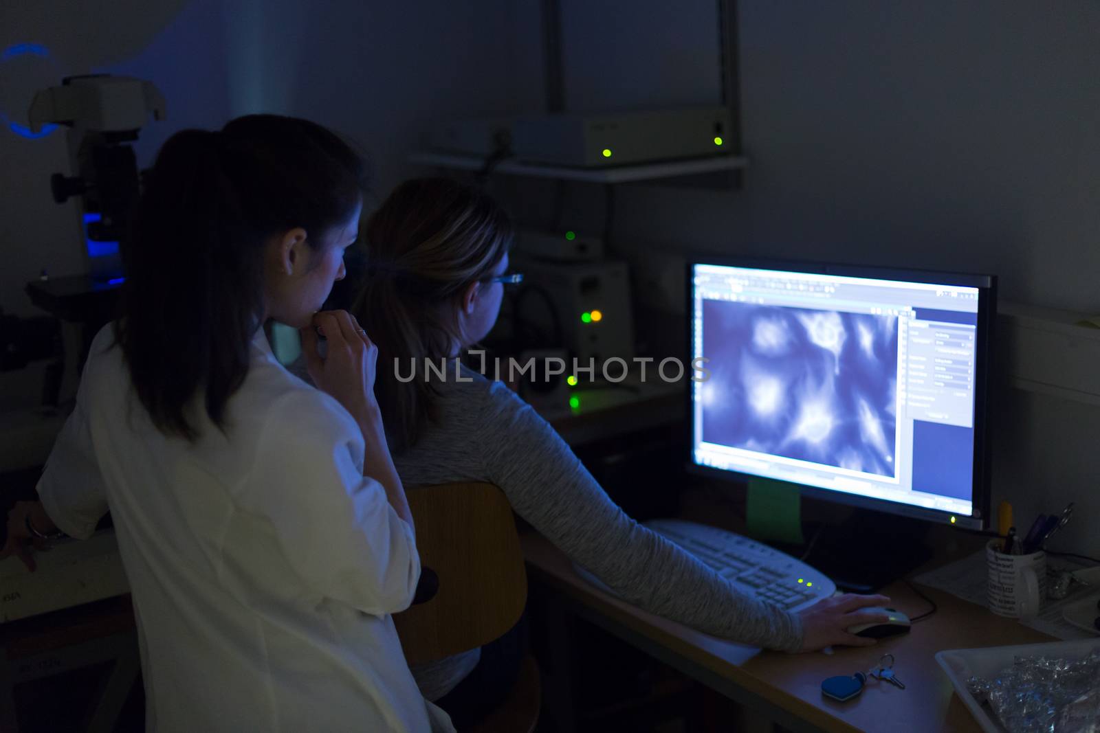 Life science female researchers microscoping with hi-tech fluorescent microscope in scientific genetic laboratory. Healthcare and biotechnology.