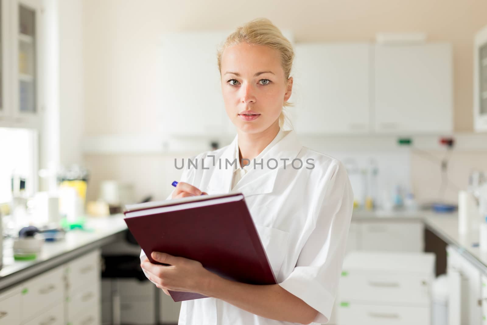 Portrait of young, confident female health care professional taking notes during inventory in scientific laboratory or medical doctors office by kasto