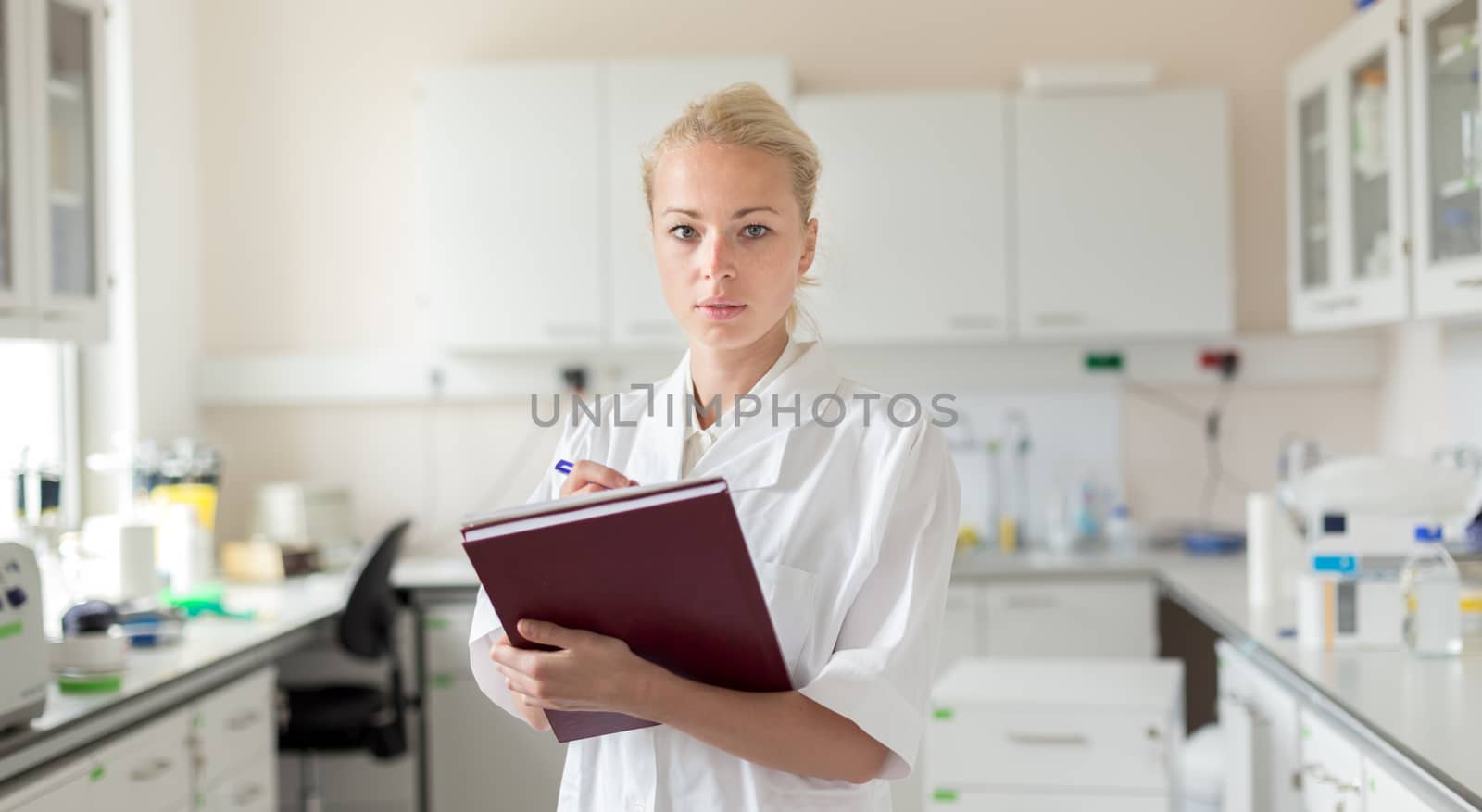 Portrait of young, confident female health care professional taking notes during inventory in scientific laboratory or medical doctors office by kasto