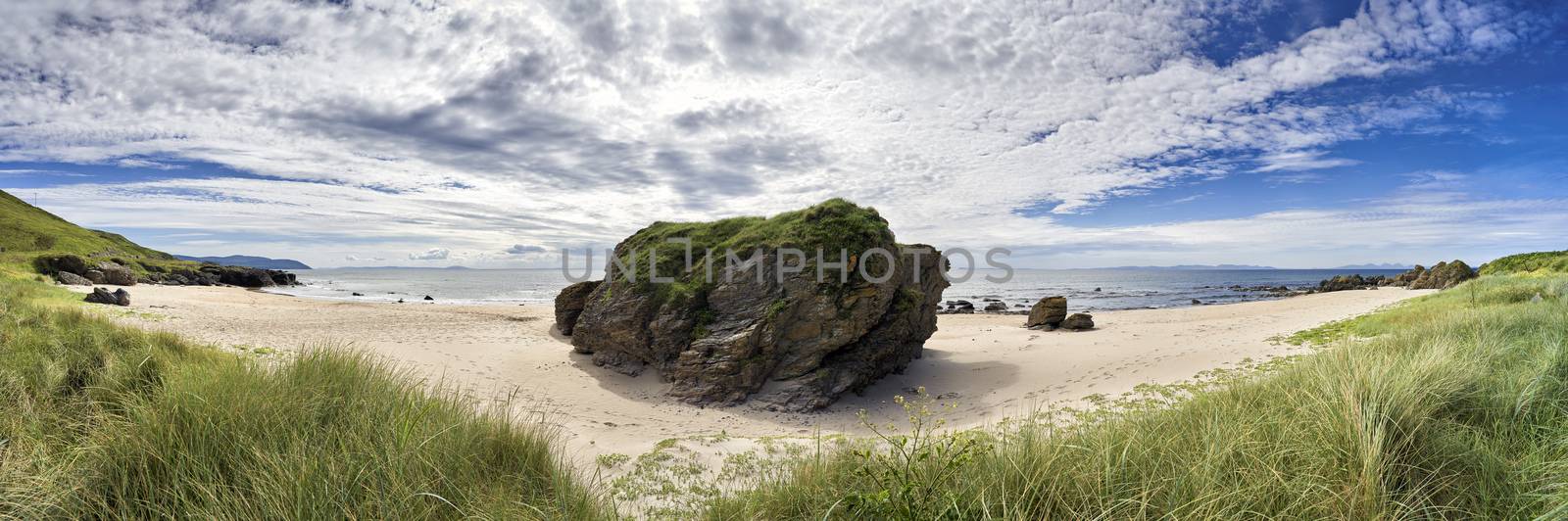 Panoramic view of beach looking out to sea on the West coast of Scotland surrounded by rocks,grass and flowers