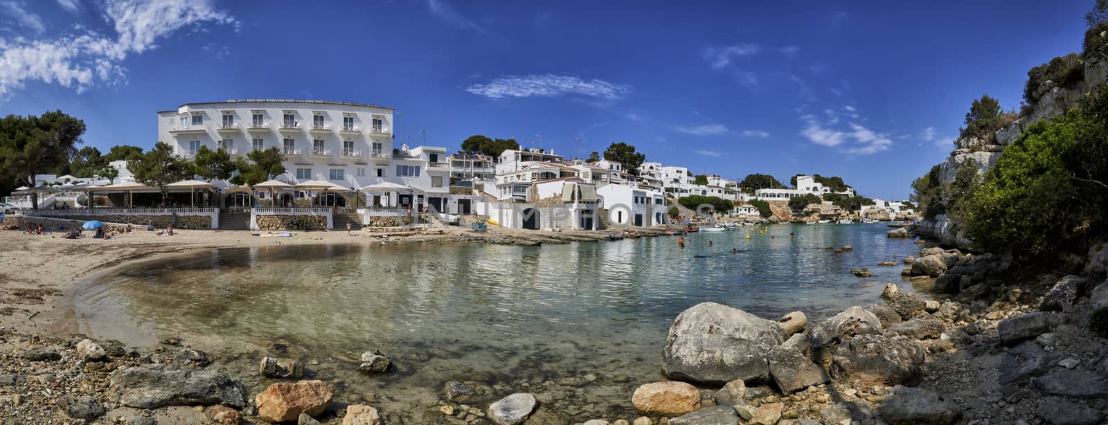 Panorama of beach,houses and small boats moored in the Mediterranean cove of Cala Alcaufar,Menorca,