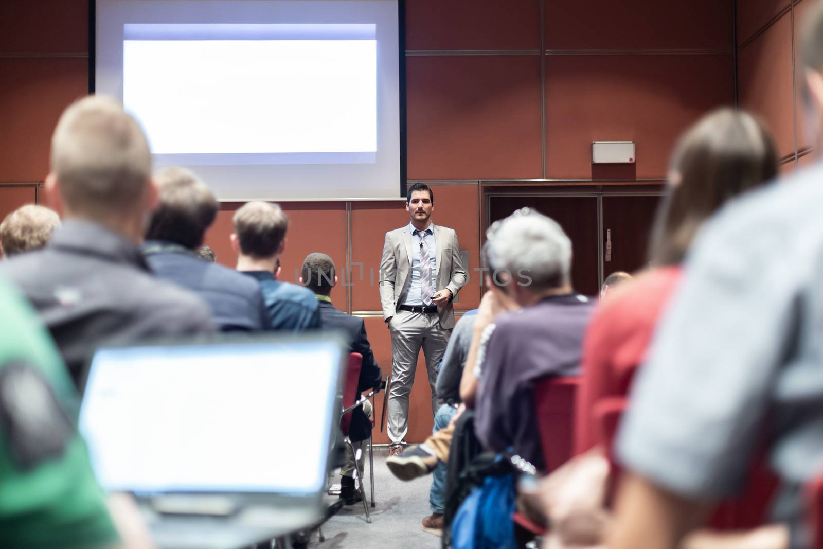 Speaker giving a talk in conference hall at business meeting event. Rear view of unrecognizable people in audience at the conference hall. Business and entrepreneurship concept.