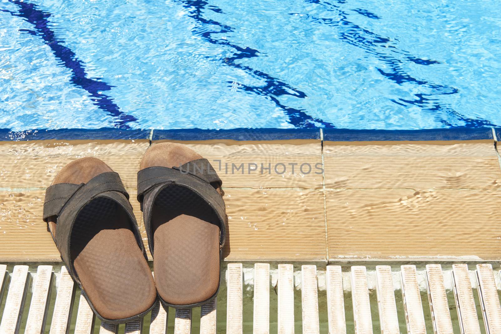 A pair of mens leather sandals by side of swimming pool