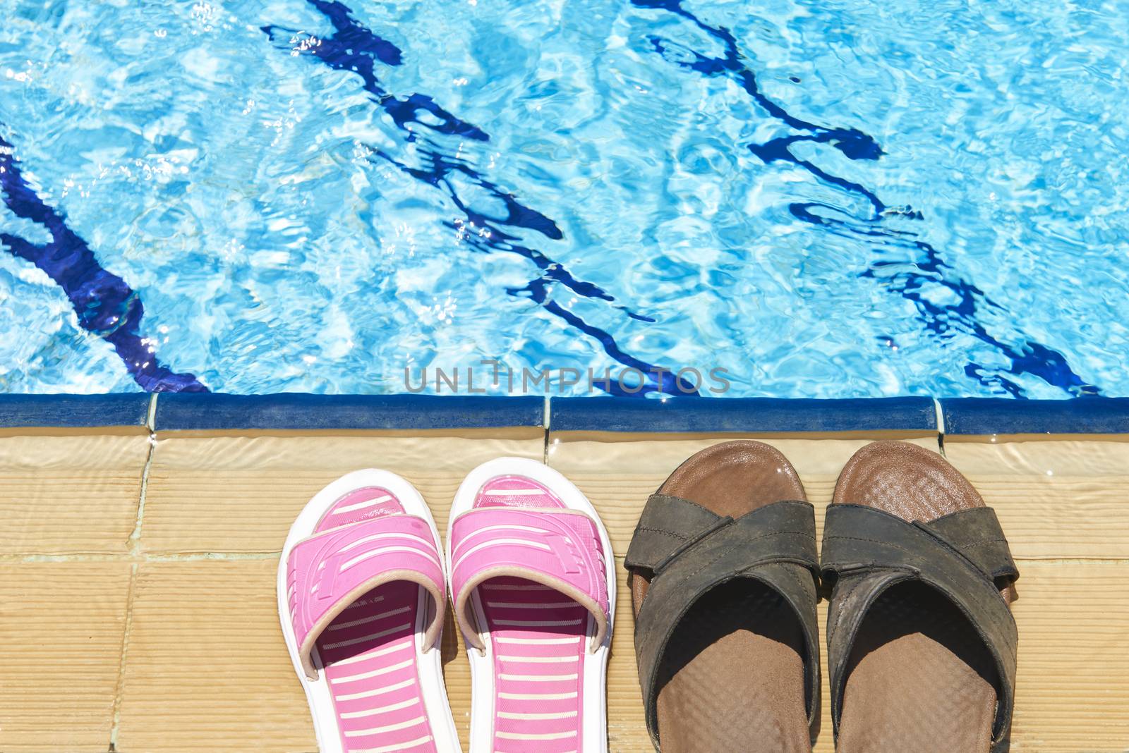 A pair of mens and womans sandals by side of swimming pool