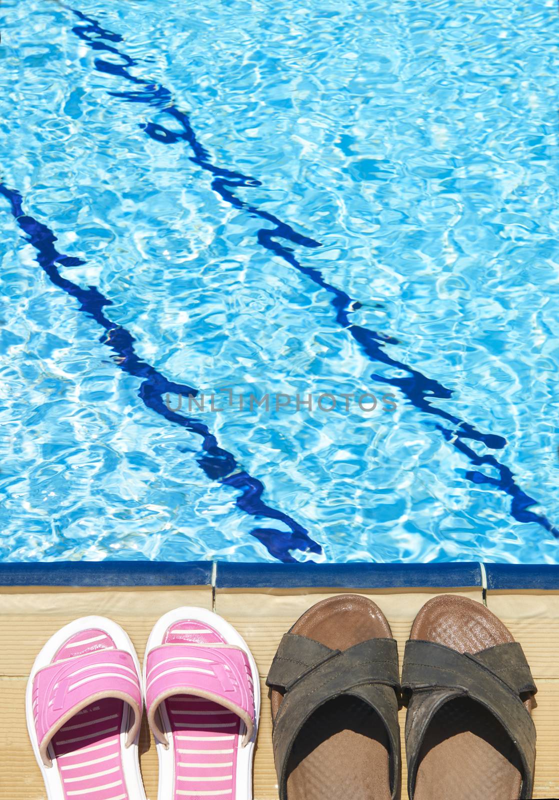 A pair of mens and womans sandals by side of swimming pool