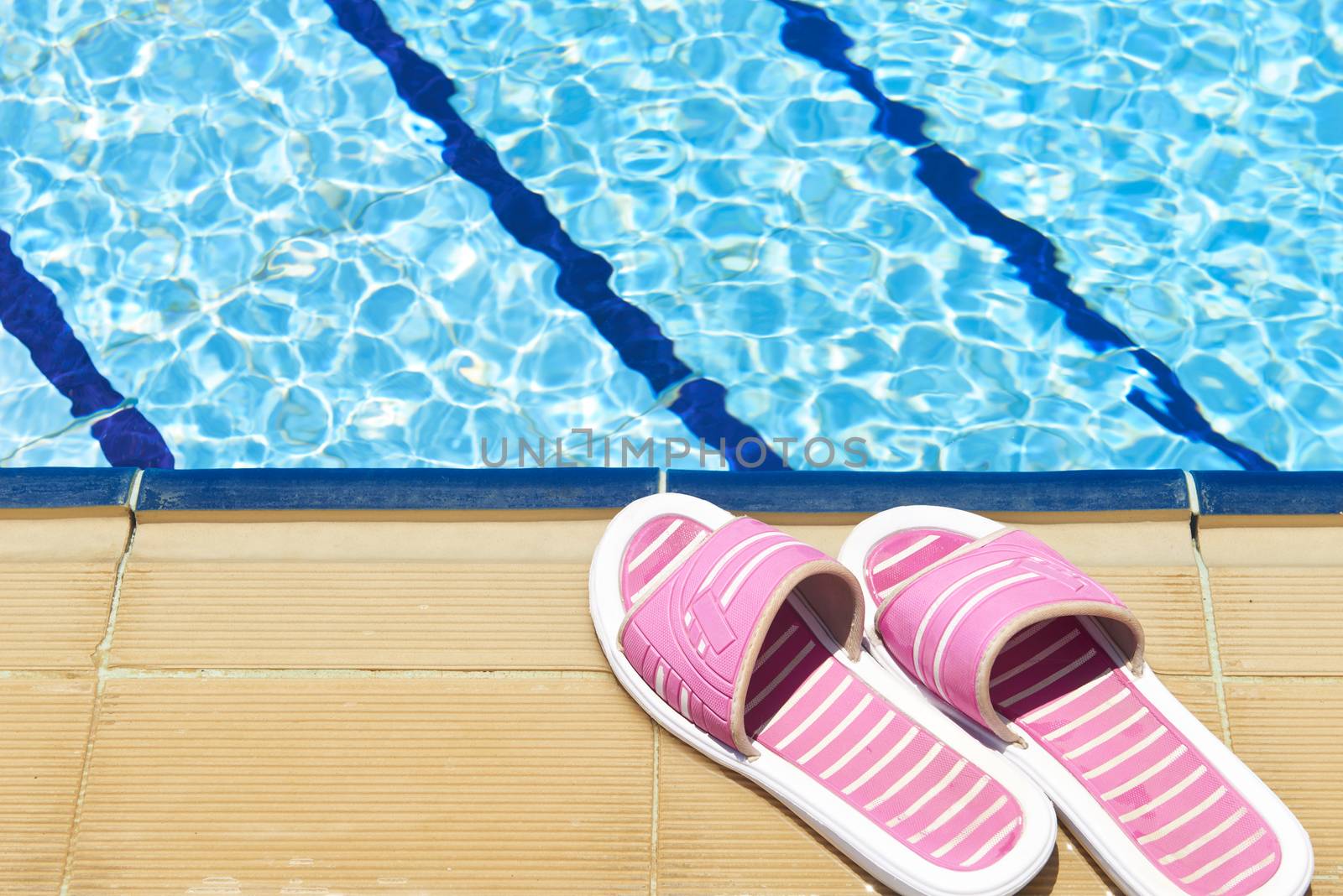 A pair of womens plastic sandals by side of swimming pool