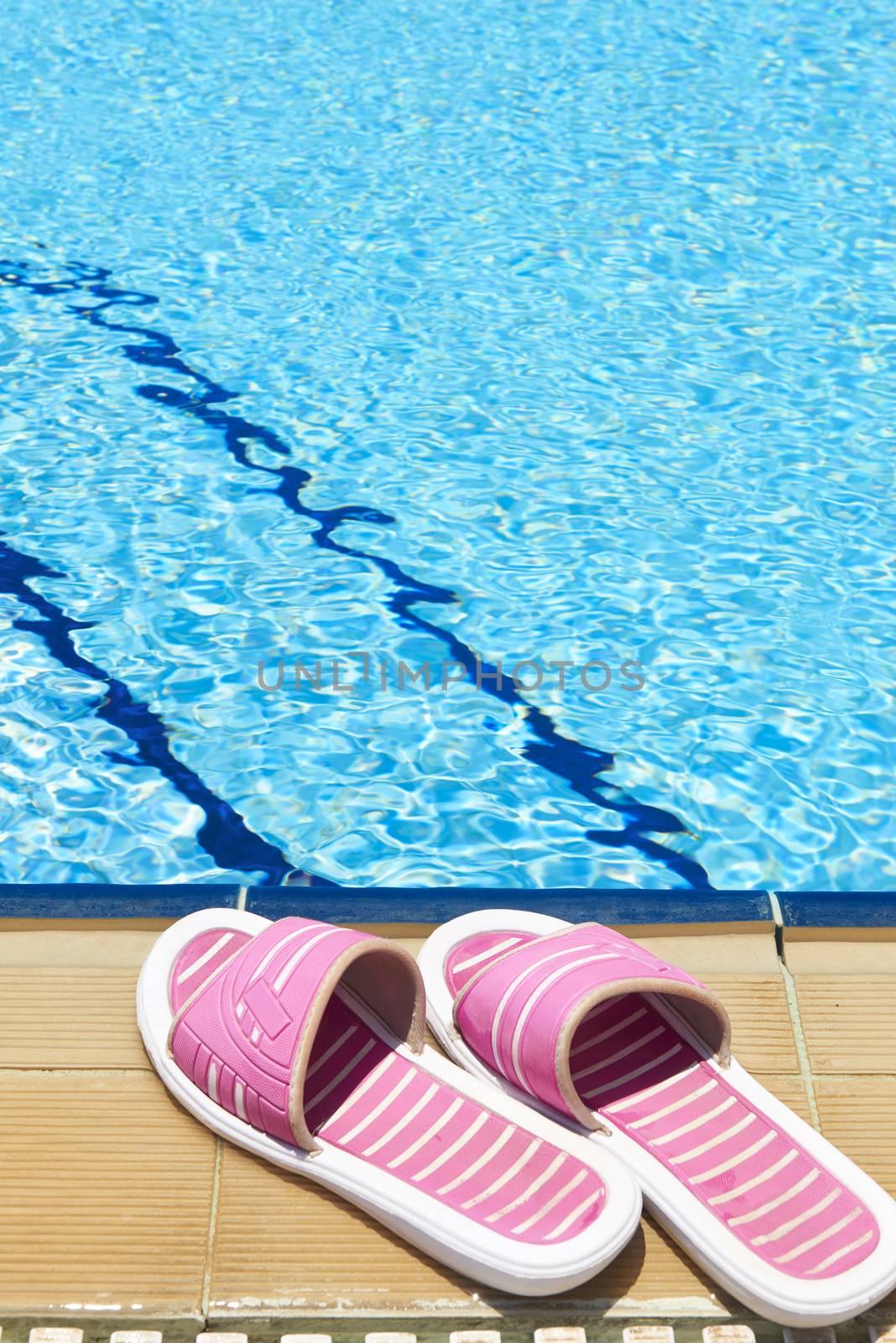 A pair of womens plastic sandals by side of swimming pool