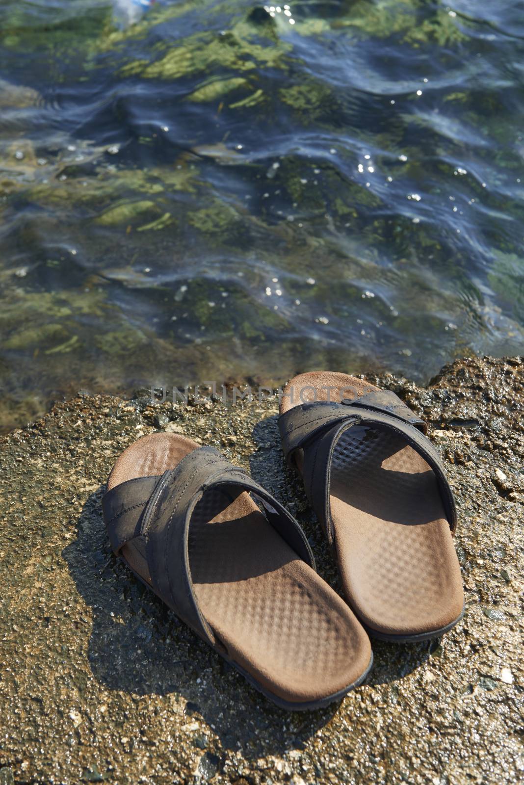 A pair of mens leather sandals on water’s edge by sea