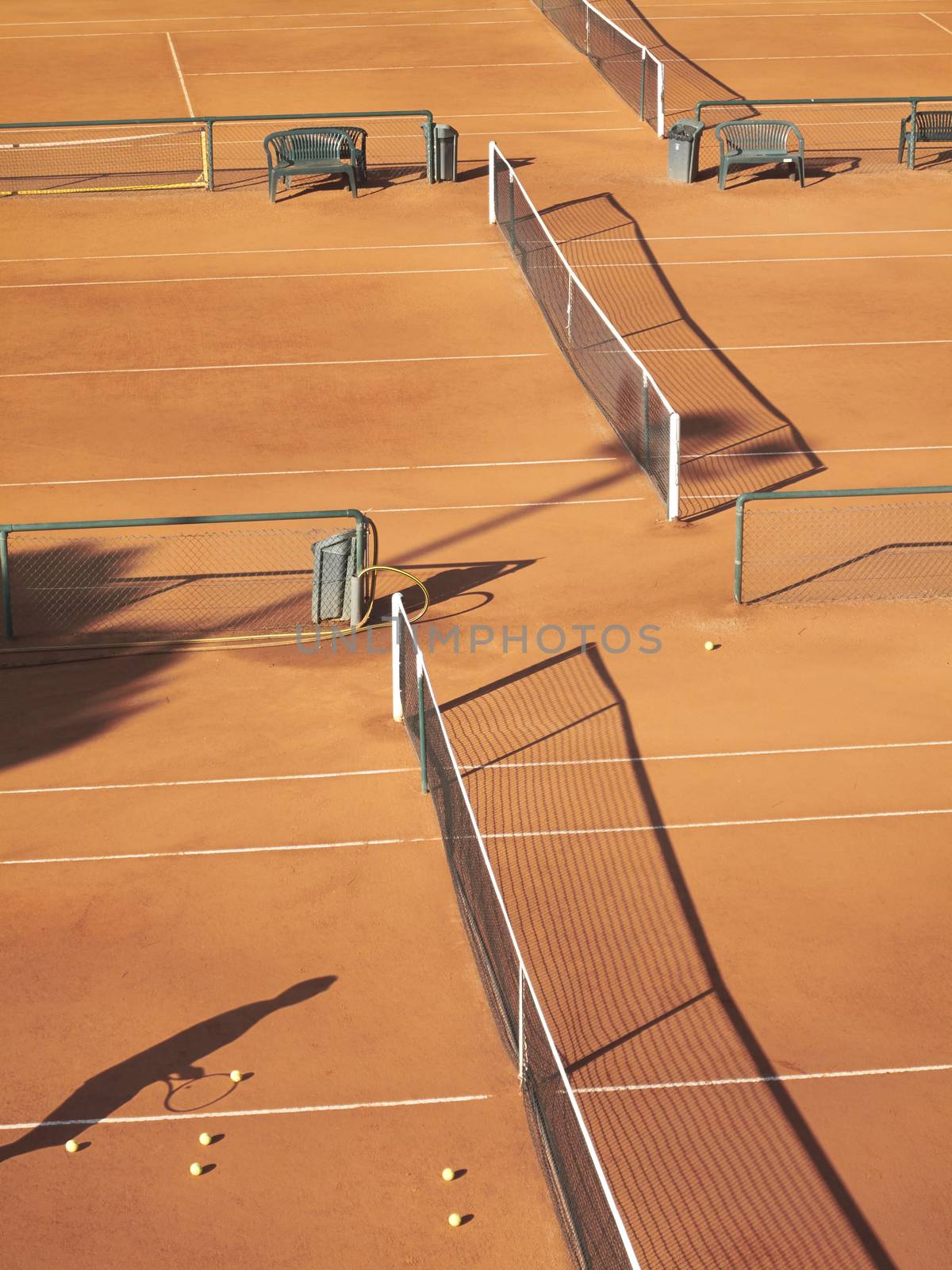 Shadow of tennis player at net with scatttered tennis balls on clay court