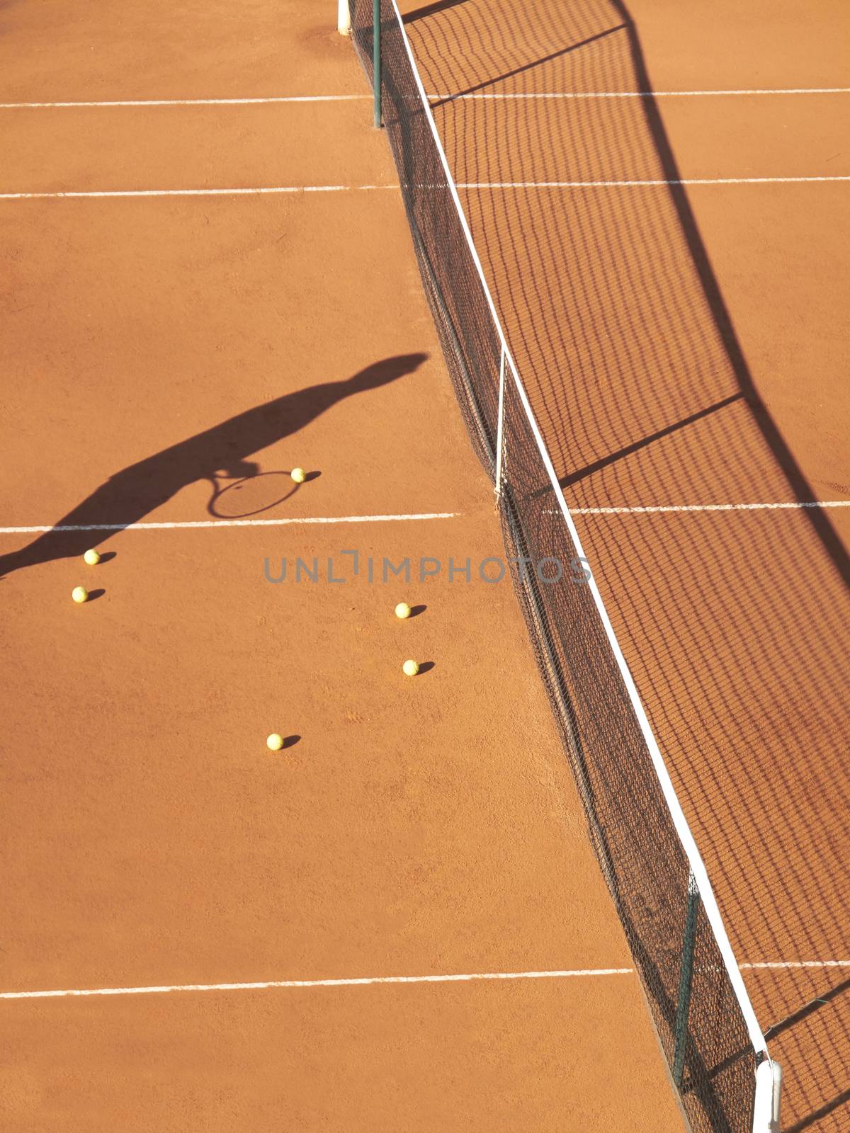 Shadow of tennis player at net with scatttered tennis balls on clay court