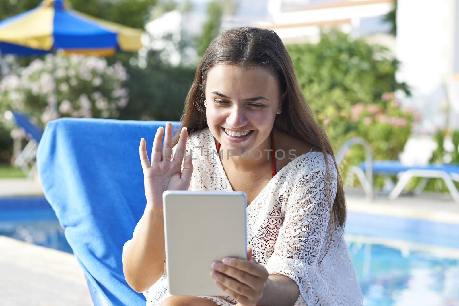 Young girl using digital tablet while relaxing by swimming pool on vacation