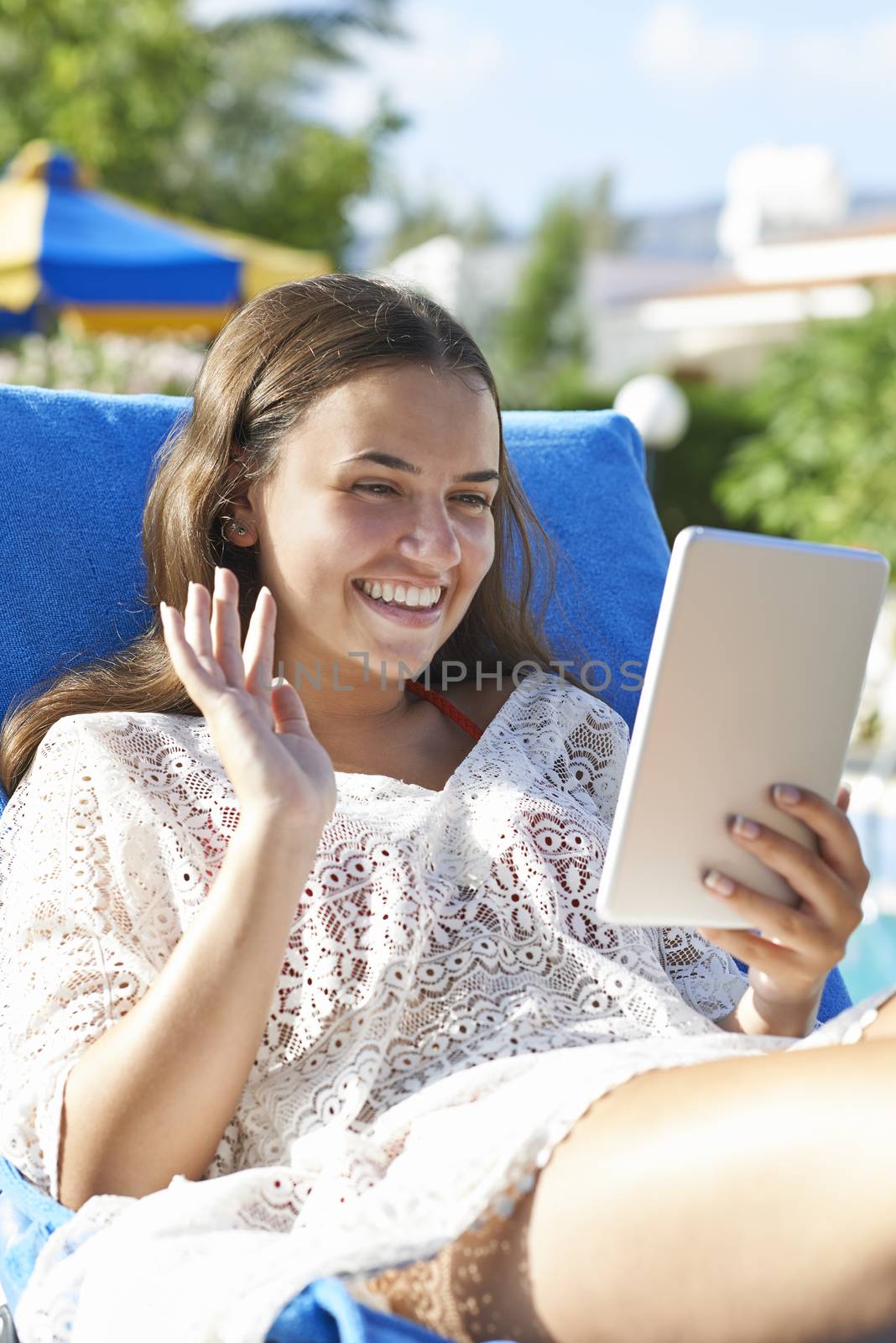 Young girl using digital tablet while relaxing by swimming pool on vacation