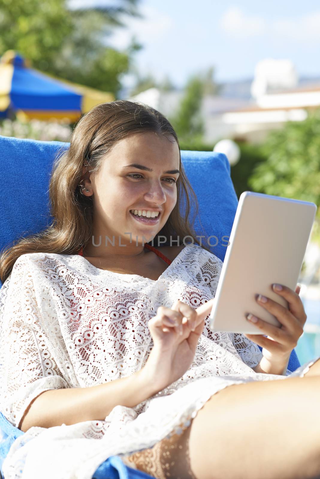 Young girl using digital tablet while relaxing by swimming pool on vacation