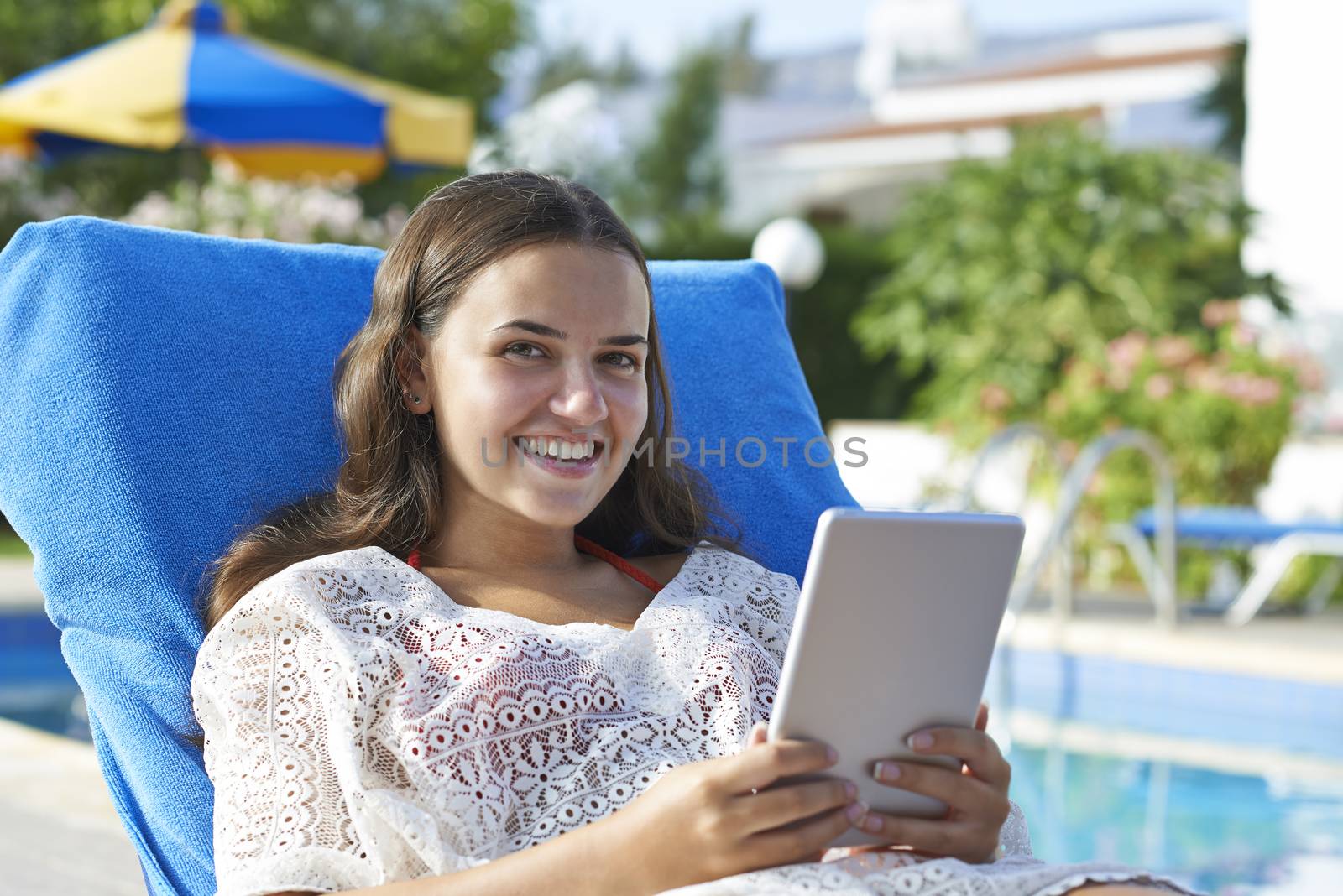 Young girl using digital tablet while relaxing by swimming pool on vacation