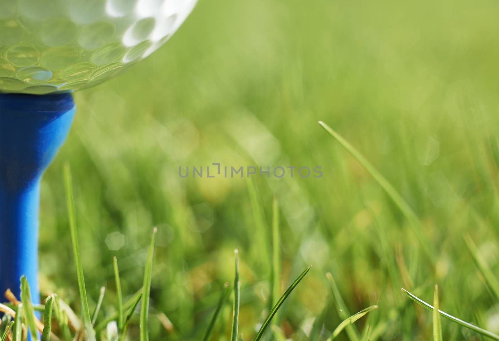 Close-up of golf ball resting on blue tee with grass and space for copy