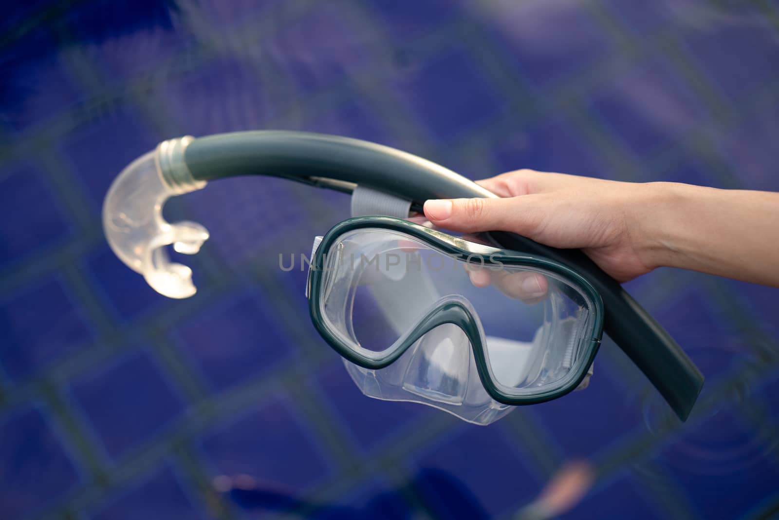Hand with equipment for snorkeling mask at the pool.