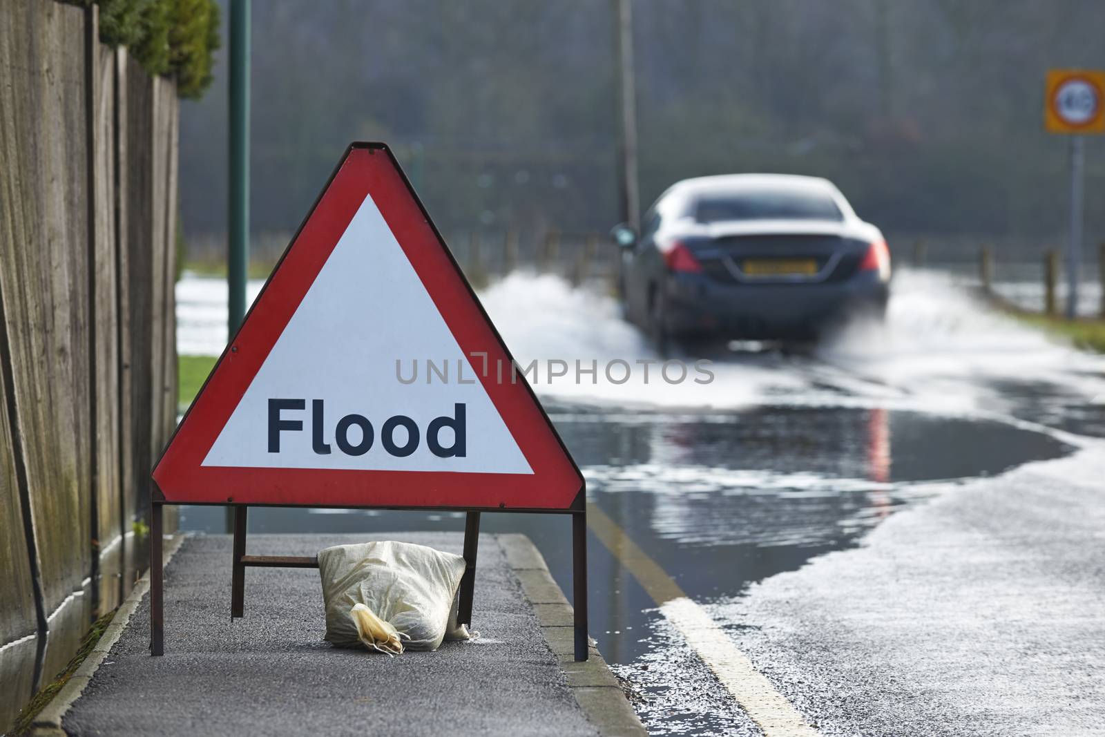 Motorist driving through flood waters with warning sign in foreground