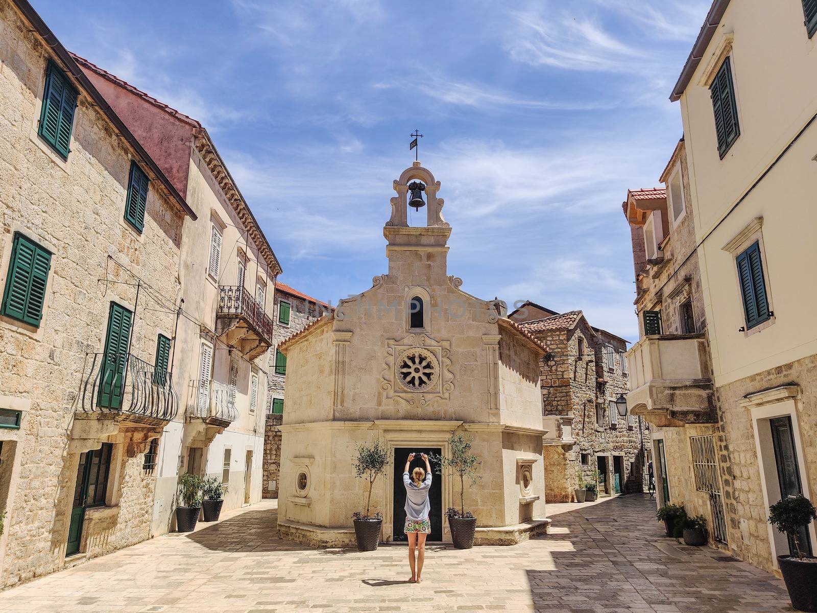 Female tourist taking photo of mall church on square of small urban village of Stari grad on Hvar island in Croatia, Adriatic Sea, Europe.