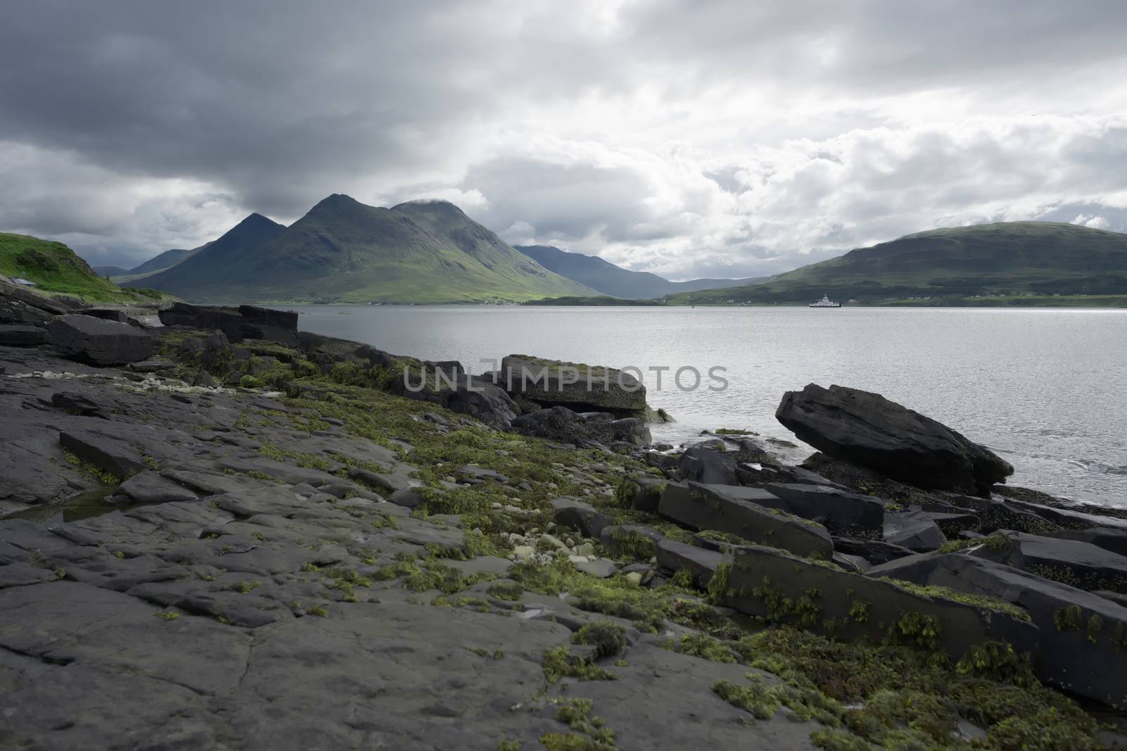 Coastal landscape from the isle of raasay looking towards the isle of skye. Ferry travels the sea under the peak of Glamaig which is cloud topped.